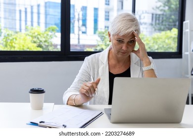 Business Woman Using Digital Table And Working On Laptop Computer In Modern Home Office.  Senior Woman Serious Working On Laptop. Serious Mature Older Adult Woman Watching On Laptop Working From Home.