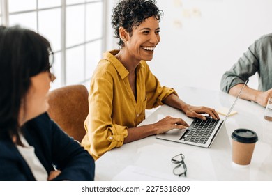 Business woman using a laptop in a boardroom meeting. Professional business woman sitting in a boardroom with her colleagues. Business people discussing a project in an office.