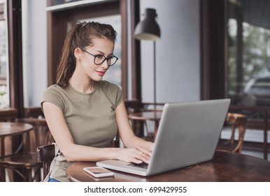 Business Woman Using Laptop At Cafe. Young Beautiful Girl Sitting In A Coffee Shop And Working On Computer