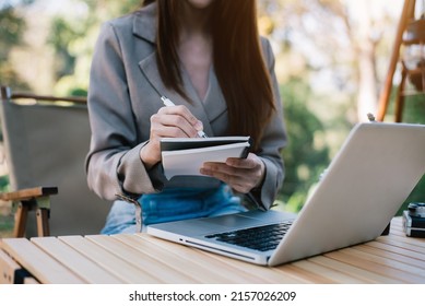 Business woman using laptop to work and writing on notebook with pen with mobile next to laptop. - Shutterstock ID 2157026209