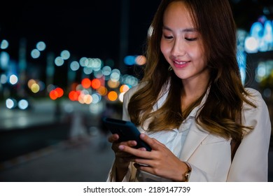 Business Woman Using Mobile Phone Walking Through Night City Street While Waiting Car To Pick Up Home, Beautiful Young Smiling Female Texting Work On Smartphone, Social Media