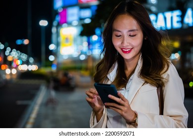 Business Woman Using Mobile Phone Walking Through Night City Street While Waiting Car To Pick Up Home, Beautiful Young Smiling Female Texting Work Message On Smartphone Outside Office, Social Media