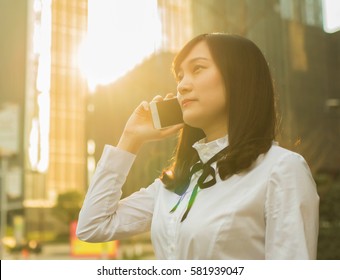 business woman using mobile phone during sunset in front of modern building