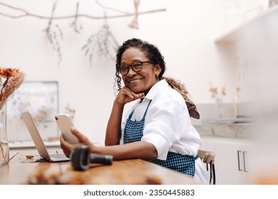 Business woman using mobile technology to manage and run her floral startup, staying on top of orders and inventory with ease. Mature black craftswoman operating a flower shop. - Powered by Shutterstock