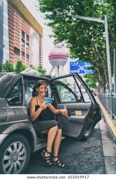 Business woman using\
phone app for mobile payment of ride share black cab car. Rideshare\
sharing concept. Asian businesswoman in financial district Pudong,\
Shanghai, China.
