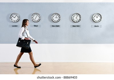 Business Woman Walking In A Hurry Past A Row Of Clocks Showing The Time In Various Parts Of The World. Business, Travel, Time Concept