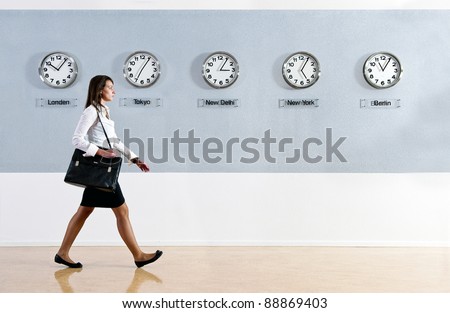Business woman walking in a hurry past a row of clocks showing the time in various parts of the world. Business, travel, time concept
