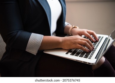 Business woman wearing black jacket and gold wrist watch using laptop on her lap