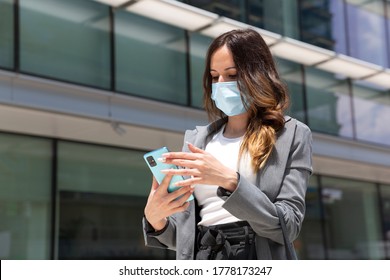 Business woman wearing a face mask looking at her smartphone next to an office building. Selective focus. Space for text. New normal concept.  - Powered by Shutterstock