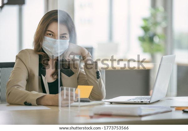 Business woman wearing face mask and\
using partition on table for protect coronavirus covid-19 pandemic.\
Social and business distancing new normal\
lifestyle.