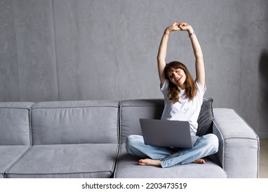 Business woman wearing white shirt sitting on sofa with laptop raising her arms above her head stretching after sitting for a long time at work. - Shutterstock ID 2203473519