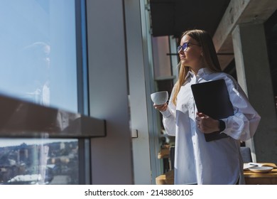 Business Woman In A White Shirt And Glasses With A Laptop In Her Hands In The Office By The Window. Modern Businesswoman In Stylish Clothes. Freelance Girl Working Outside The Office