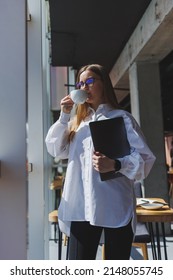 Business Woman In A White Shirt And Glasses With A Laptop In Her Hands In The Office By The Window. Modern Businesswoman In Stylish Clothes. Freelance Girl Working Outside The Office