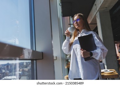 Business Woman In A White Shirt And Glasses With A Laptop In Her Hands In The Office By The Window. Modern Businesswoman In Stylish Clothes. Freelance Girl Working Outside The Office