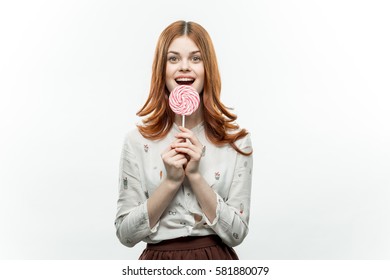 business woman in a white shirt on a light background with a large round striped candy in the hands smiling.