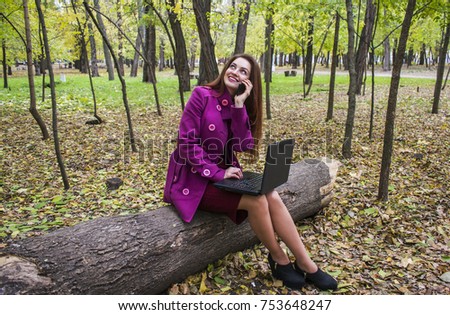 Business woman working with laptop and phone in autumn park. The woman has red hair and big green eyes. Beautiful autumn park