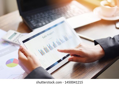 Business woman working in office with checking business report using tablet computer technology laptop with calculator and coffee cup / Sale report money analyzing graphs chart - Shutterstock ID 1450041215