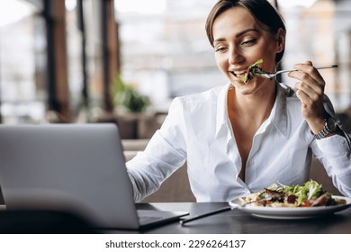 Business woman working on laptop and eating salad - Powered by Shutterstock