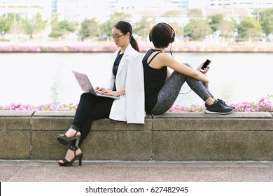 Business woman working on the laptop computer sitting near the relaxing sport woman in city park, Life balance concept, Workaholic and healthy lifestyle.