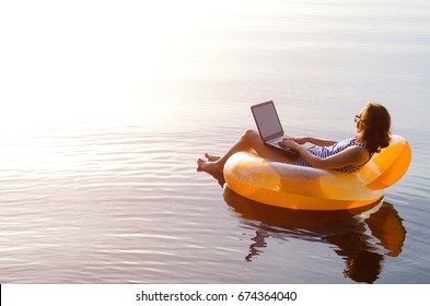 Business woman working on a laptop in an inflatable ring in the water, a copy of the free space. Workaholic, work on vacation. - Shutterstock ID 674364040