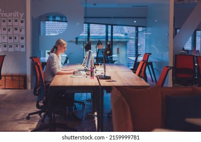 business woman working overtime alone at his desk on a desktop computer in an open space modern coworking office - Shutterstock ID 2159999781