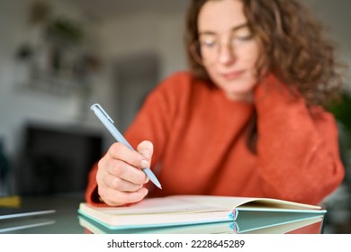 Business woman or young female student holding pen in hand writing in paper notebook journal, taking notes studying, doing homework, making checklist. Close up view