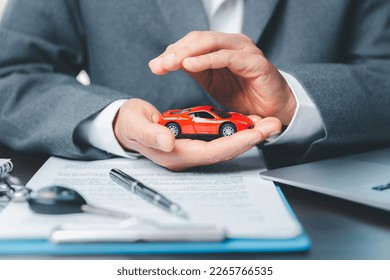 Business woman's hand protecting red toy car on desk. Planning to manage transportation finance costs. Concept of car insurance business, saving buy - sale with tax and loan for new car.