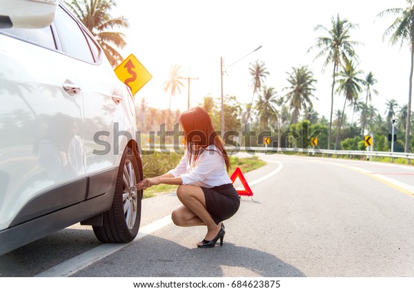 Business\
women driver changing tyre on her broken\
car.