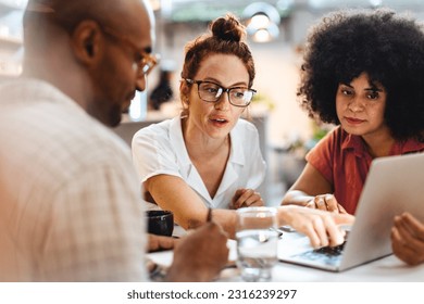 Business women having a work lunch in a café, exchanging ideas and discussing their projects with a client. Young business team using a laptop as they sit around a coffee table. - Powered by Shutterstock