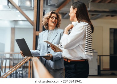 Business women smiling as they have a meeting on a balcony. Professional business women discuss their upcoming work and ways to get it done. Women working together in a female-led startup. - Powered by Shutterstock