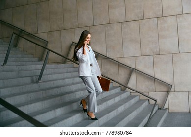 Business Women Style. Woman Going To Work Talking On Phone While Going Downstairs. Portrait Of Beautiful Smiling Female In Stylish Clothes Calling Someone While Going Down Stairs. High Resolution.
