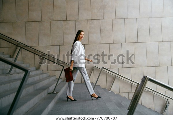 ビジネス ウーマン スタイル 下を歩いて仕事に行く女性 階段を降りるスタイリッシュなオフィス服を着た美しい微笑む女性のポートレート 高解像度 の写真素材 今すぐ編集