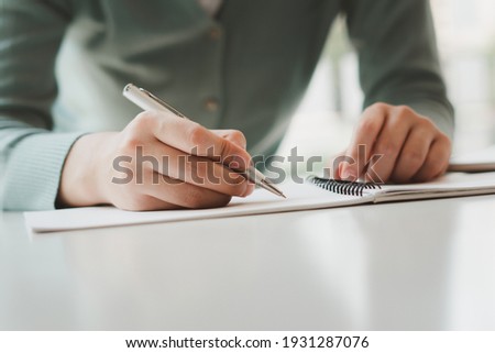 Business women write on notepad with pen to calculate financial statements within the office.