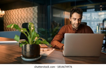 Business Working On A Laptop And Going Over Paperwork While Sitting At His Desk In A Quiet Office After Hours