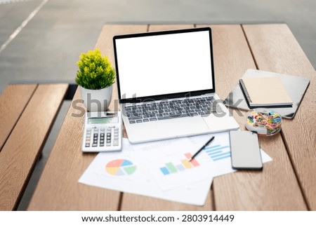 Business workspace flatlay featuring an open laptop mockup with blank screen surrounded by financial charts, calculator, notebook, and smartphone for corporate use.