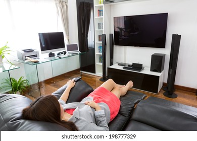 Business young woman watching TV in modern home office with computer and laptop
