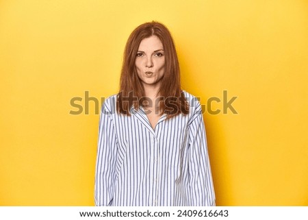 Business-dressed redhead, formal studio shot blows cheeks, has tired expression. Facial expression concept.