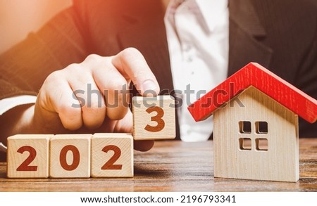 Businessman and 2023 blocks near house. Forecast of real estate prices on the new year. Trends and changes, new challenges for the economy and the impact on housing market. Mortgage loan rates.