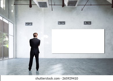 businessman in 3D rendered empty space, looking at a wall with a blank canvas - Powered by Shutterstock