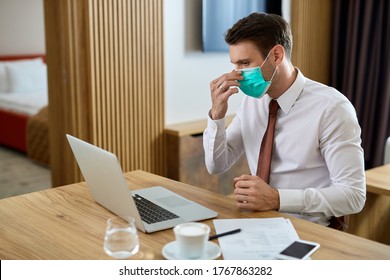 Businessman Adjusting Protective Face Mask While Working On A Computer In Hotel Room. 