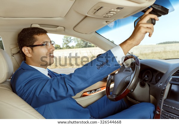 Businessman adjusting the rearview mirror while\
driving a car