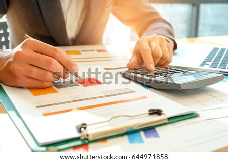 Businessman analyzes graph data and use the calculator to calculate the cost,Office worker is analyzing graphs and using a calculator.