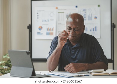 Businessman analyzing data on a tablet at desk with charts in the background, office setting, thoughtful expression while working. - Powered by Shutterstock