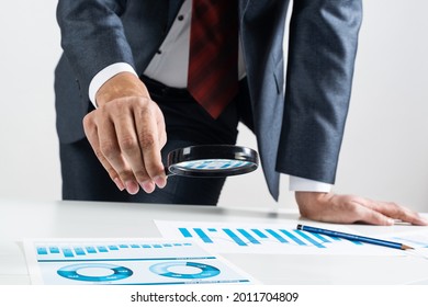 Businessman Analyzing Financial Documents With Magnifying Glass In Hand. Financial Expertise And Consulting. Manager In Suit And Tie Working With Business Analytics. Entrepreneurship And Leadership.