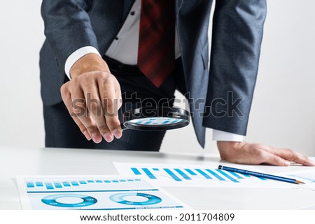 Businessman analyzing financial documents with magnifying glass in hand. Financial expertise and consulting. Manager in suit and tie working with business analytics. Entrepreneurship and leadership.