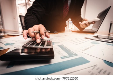 A businessman analyzing investment charts at workplace and using calculator for calculate finance in office.