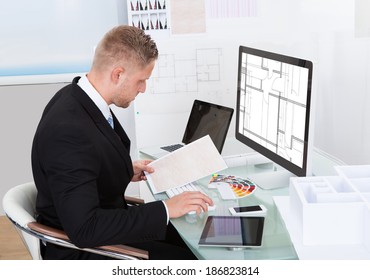 Businessman analyzing a spreadsheet online checking against a document in his hand to collate the information - Shutterstock ID 186823814