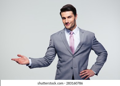 Businessman with arm out in a welcoming gesture over gray background - Powered by Shutterstock