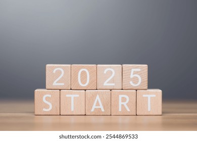 A businessman arranges wooden blocks spelling out 'START 2025' on a table, symbolizing the beginning of new goals and ventures for the upcoming year. Image reflects motivation and forward planning - Powered by Shutterstock