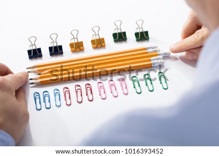 Businessman Arranging The Pencils In Between The Row Of Colorful Pins And Paper Clips